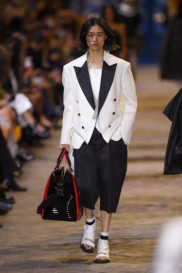 A model walking in a white blazer and and black pants at the Louis Vuitton Womenswear Spring/Summer ...