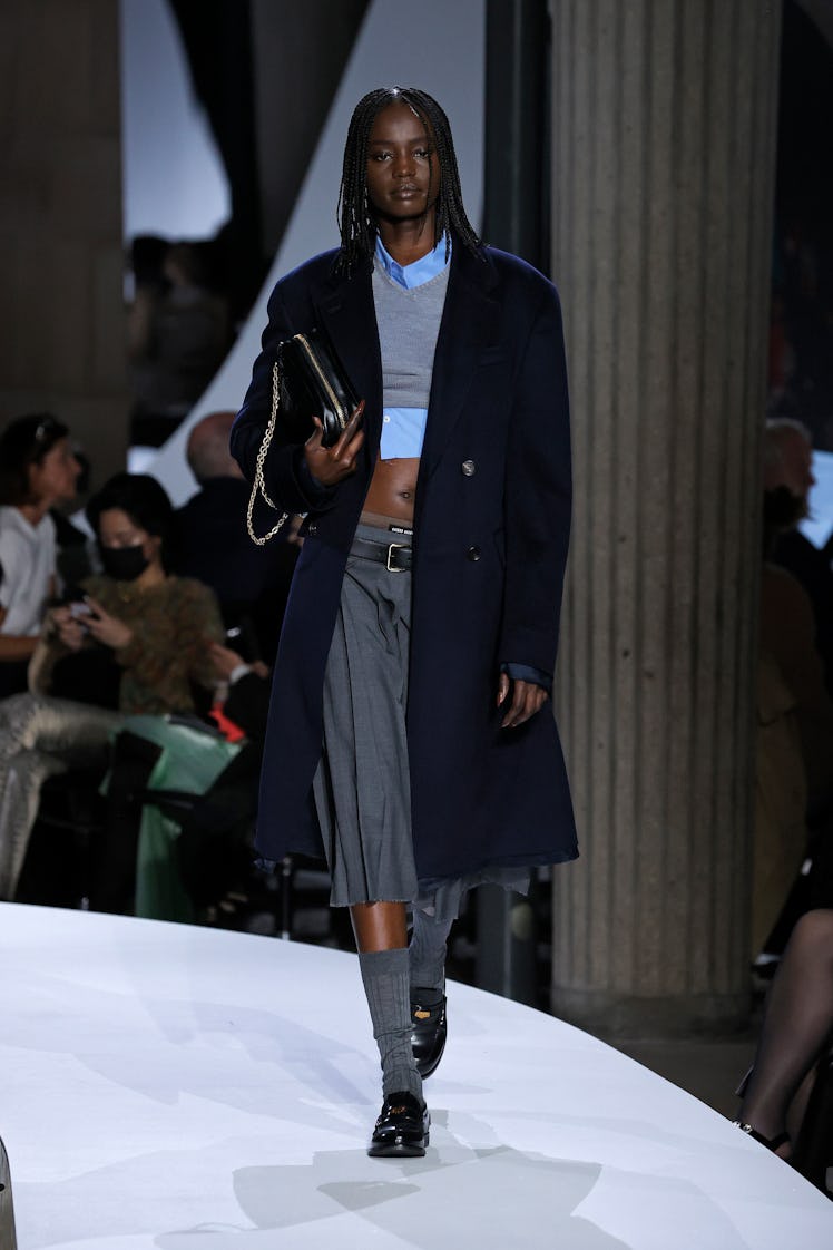A model walking in a in a black coat, grey top and skirt at the Miu Miu Womenswear Spring/Summer 202...