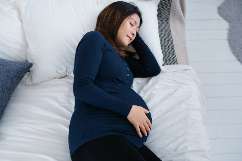 Image of a pregnant adult lying down in bed while resting a hand on the belly. 