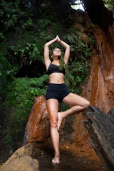 A woman in tree pose under a waterfall. The October new moon's spiritual meaning suggests a fresh st...