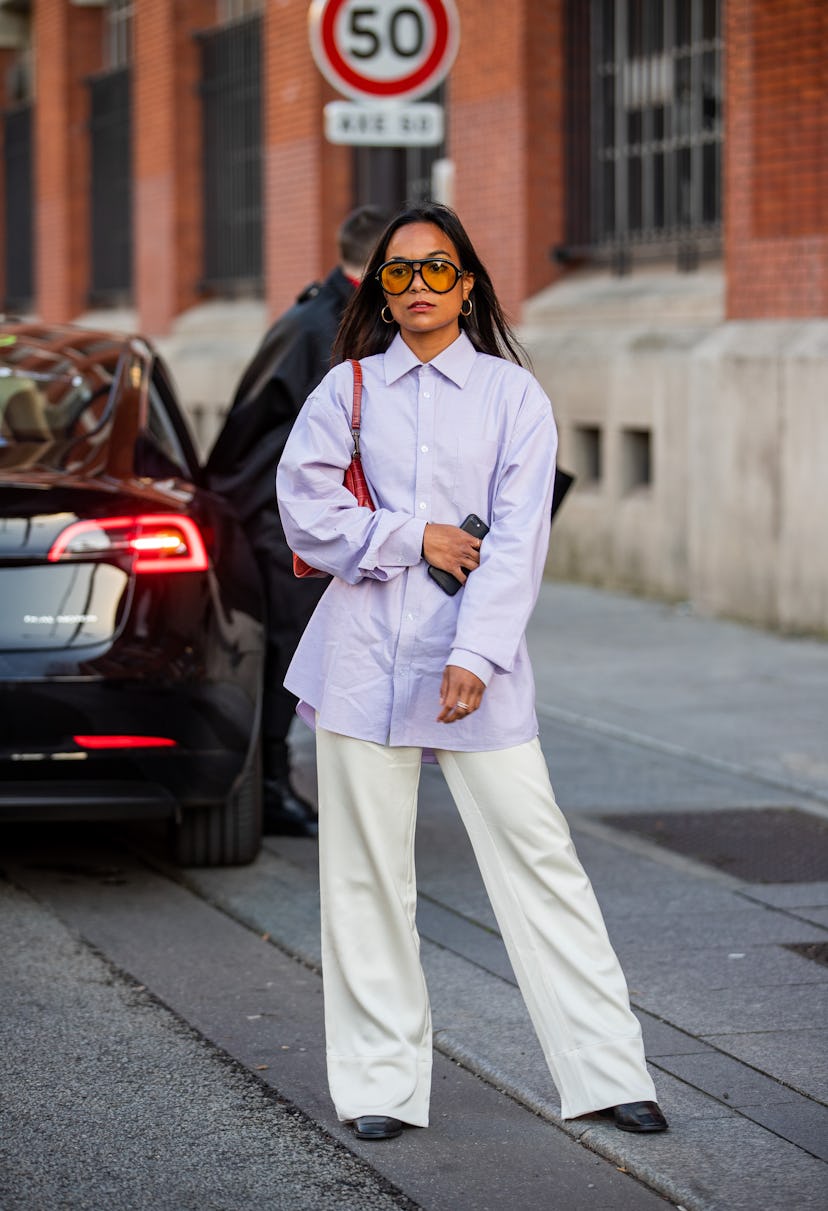 PARIS, FRANCE - SEPTEMBER 29: A guest is seen wearing rose button shirt, red bag, creme white pants ...