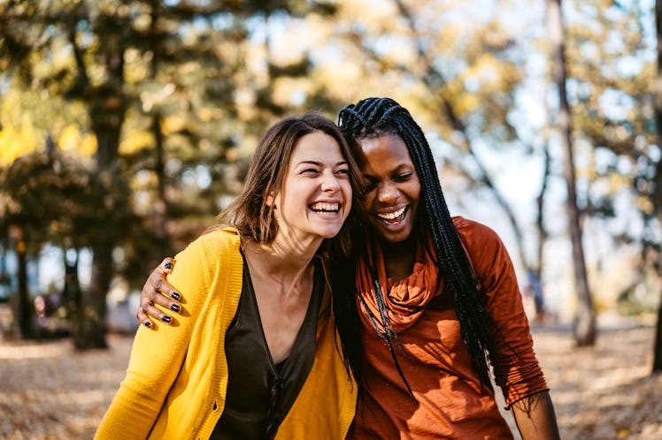 Multi-ethnic female friends embracing and laughing in public park.