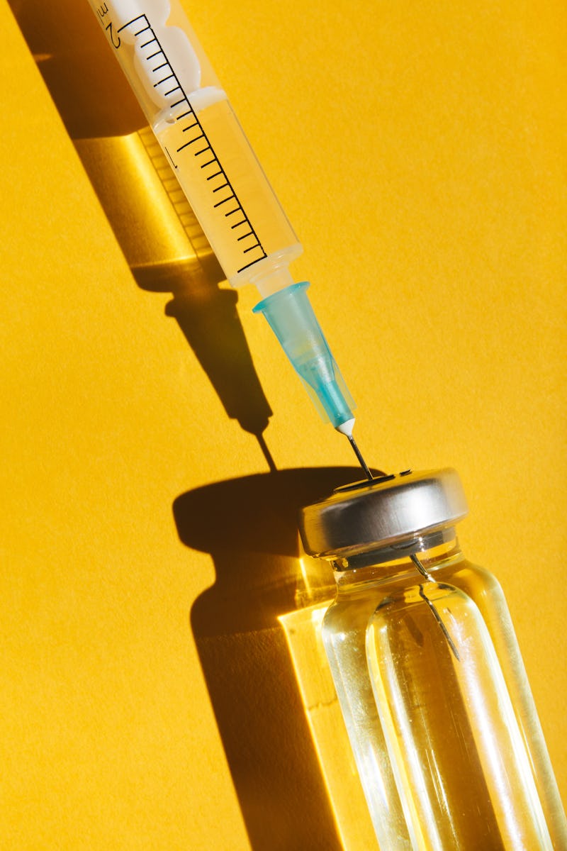 Close-up vial and syringe with a vaccine on yellow background. Concept of medical treatment or vacci...