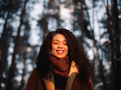 Young woman wearing coat in forest during November 2021, the best month for her zodiac sign.