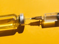 Close-up vial and syringe with a vaccine on yellow background. Concept of medical treatment or vacci...