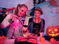 Female friends having fun and drinking TikTok drinks inspired by Halloween movies at the Halloween p...