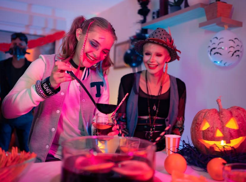 Female friends having fun and drinking TikTok drinks inspired by Halloween movies at the Halloween p...