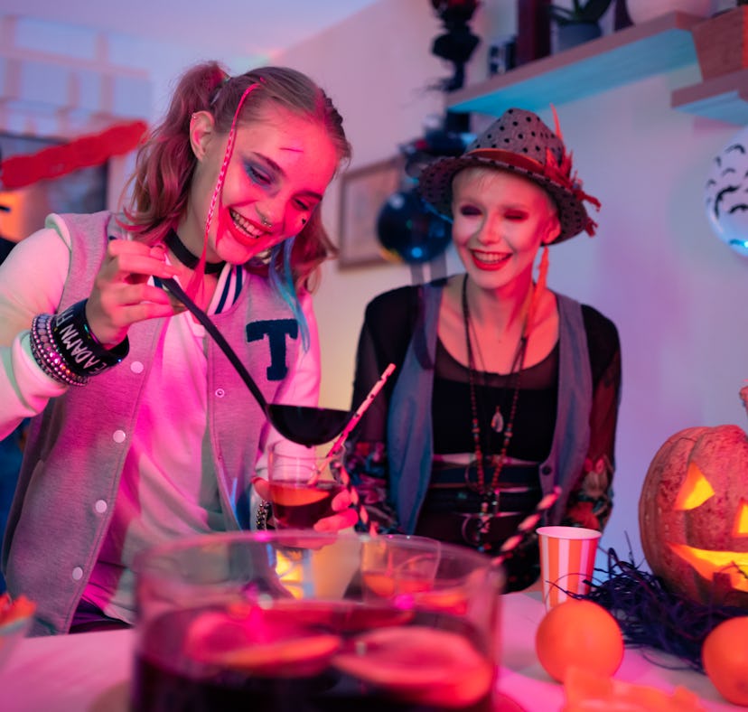 Female friends having fun and drinking TikTok drinks inspired by Halloween movies at the Halloween p...