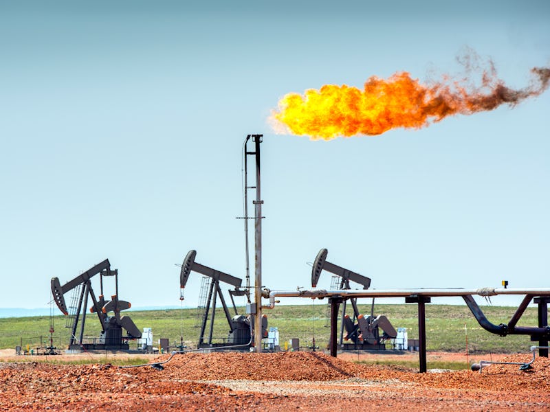 Oil well pumpjacks at work in the oil fields of North Dakota. The yellow flame is called flaring and...