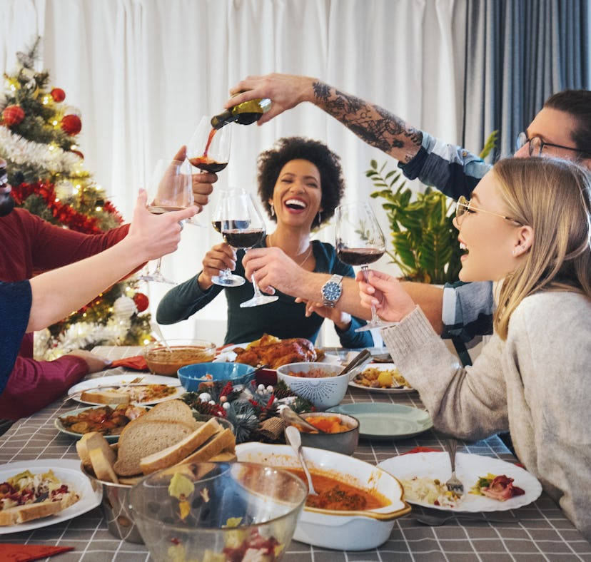 Group of friends sitting at the dinning table, eating and drinking for Thanksgiving, for which they'...