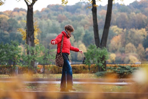 A woman in a red jacket walks among autumn leaves. Here's how the November 2021 new moon will affect...