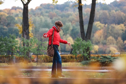 A woman in a red jacket walks among autumn leaves. Here's how the November 2021 new moon will affect...