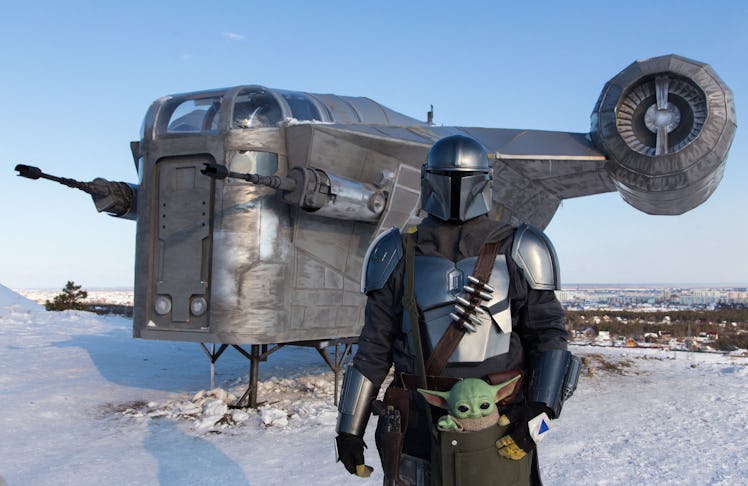 A man wearing a costume of the StarWars protagonist Din Djarin poses in front of a giant replica of ...