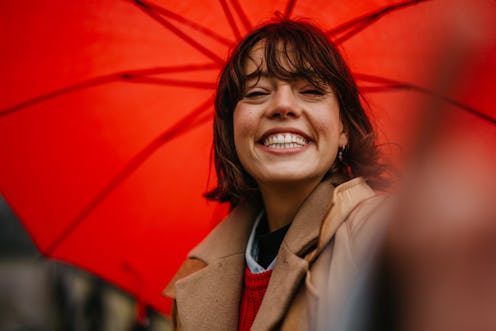 A woman takes a selfie under a red umbrella. Here's your daily horoscope for November 11, 2021.