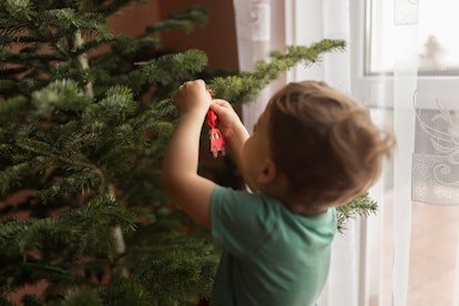 A child hanging an ornament on a Christmas tree up before Thanksgiving.