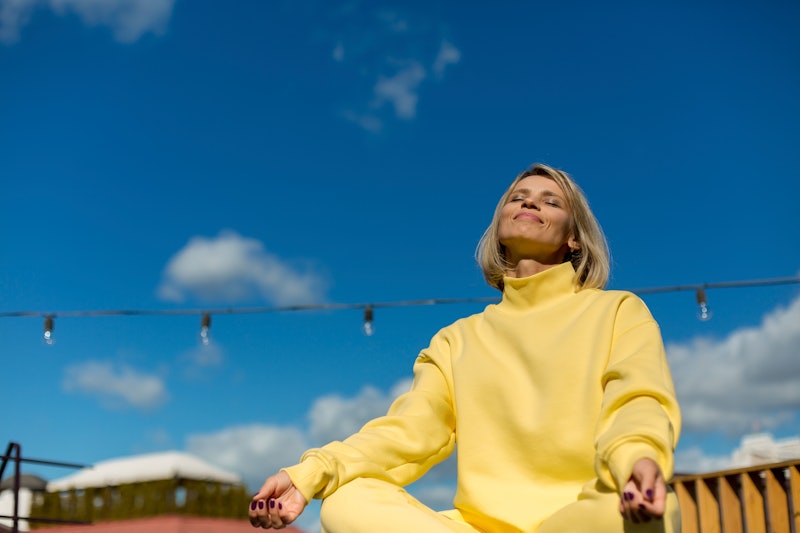 A woman in a yellow sweatshirt meditates on 11/11. Meditations for 11/11 can help you manifest on th...