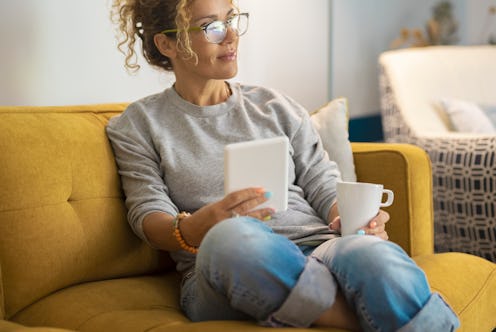 A woman sits on a couch with a cup of coffee while taking a break from Instagram.