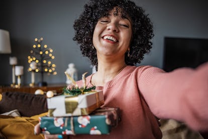 Mid adult woman at home, holding presents and looking at camera