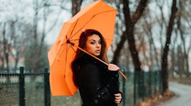 Woman holding orange umbrella in rain, thinking about how December 13, 2021 will be the worst week f...