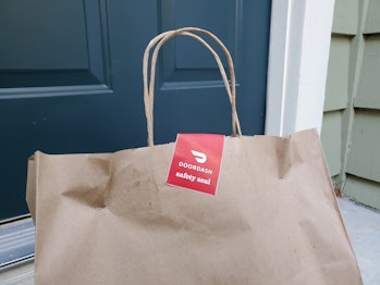 Close-up of the top of a brown paper bag, with handles and a red and white DoorDash safety seal stic...