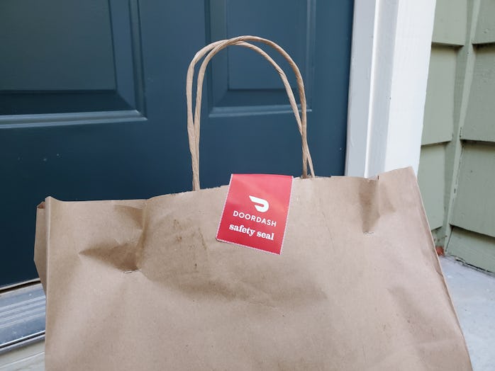 Close-up of the top of a brown paper bag, with handles and a red and white DoorDash safety seal stic...