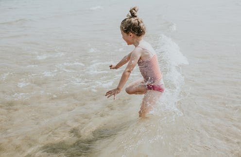 Little girl jumps in the sea, creating splashes and ripples as she cools off.