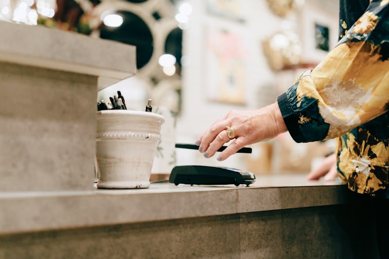 A woman pays for her purchase at a retail store by holding her smartphone over the contactless credi...