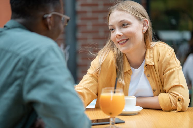 A young couple having date, drinking coffee and juice and talking at outdoor cafe.