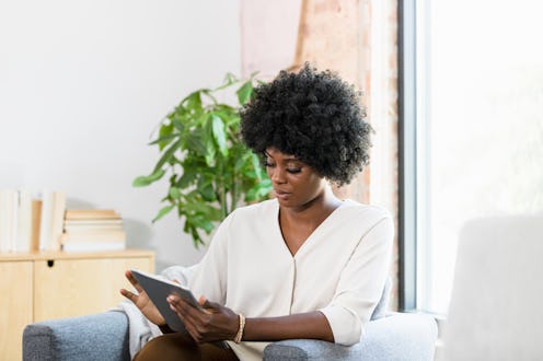 A beautiful mid adult woman concentrates as she uses a digital tablet or e-reader while sitting in a...