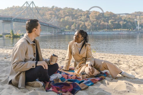 Heterosexual mix raced couple sitting on the beach on blanket and drinking coffee