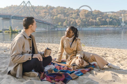 Heterosexual mix raced couple sitting on the beach on blanket and drinking coffee