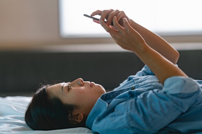 A young woman is lying on bed and sending a text to a partner.