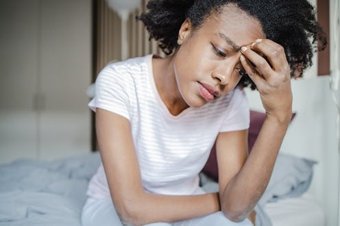 A woman in bed in her pajamas in the morning. She has a headache and feeling sad