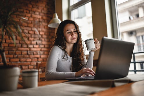 Cute Female Freelancer Working On Laptop While Drinking Coffee