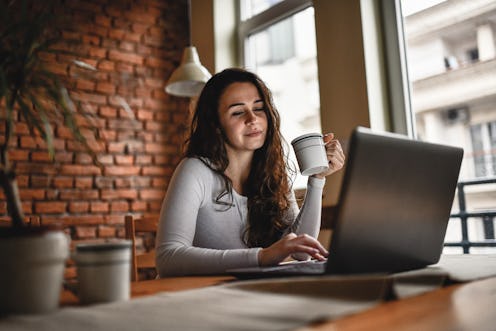 Cute Female Freelancer Working On Laptop While Drinking Coffee