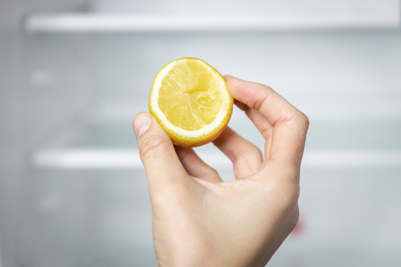 A girl's hand holds a lemon in front of an empty fridge. Food concep