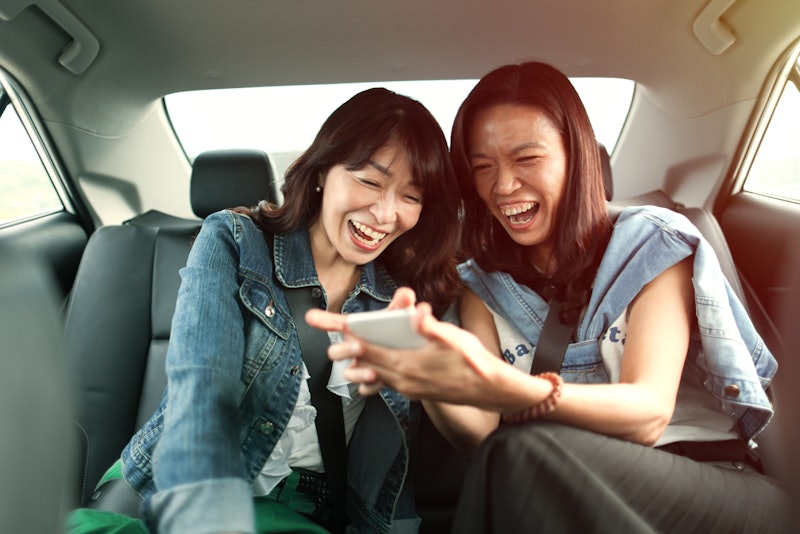Asian woman looking at smart phone with road trip friend