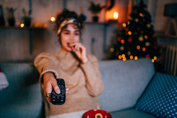 Young woman changing the channels on the TV, having the worst Christmas 2021, per her zodiac sign.