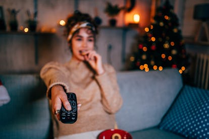 Young woman changing the channels on the TV, having the worst Christmas 2021, per her zodiac sign.