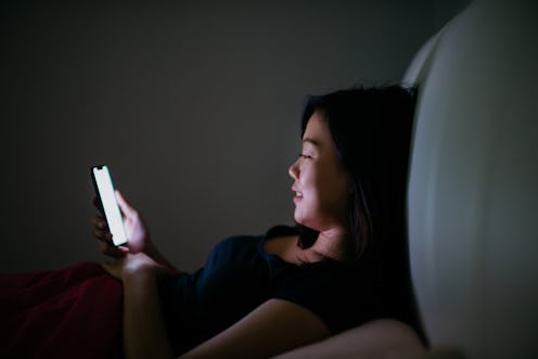 An Asian Chinese woman lying on bed and using smartphone in the dark