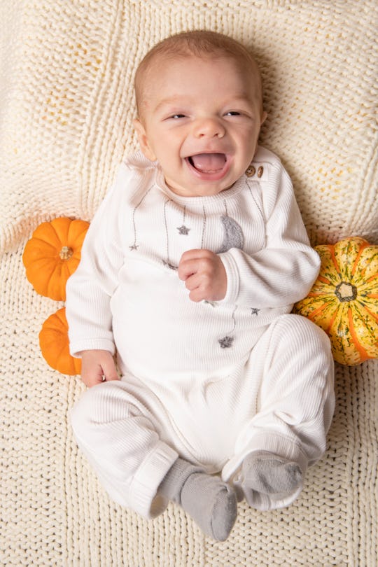 A happy 2.5 month old baby boy with a big smile as he lays on a blanket with a couple of gourds.