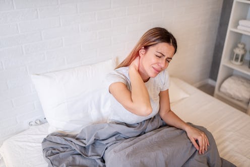 Close up of mid adult woman feeling unwell with neck pain after sleeping in bed at home.