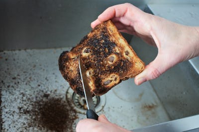 POV (point of view) of a person(female hands) holding and removing burnt from a toast with a kitchen...