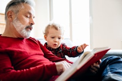 A grandpa spending some time with his grandson, sitting down and reading a Christmas book together.