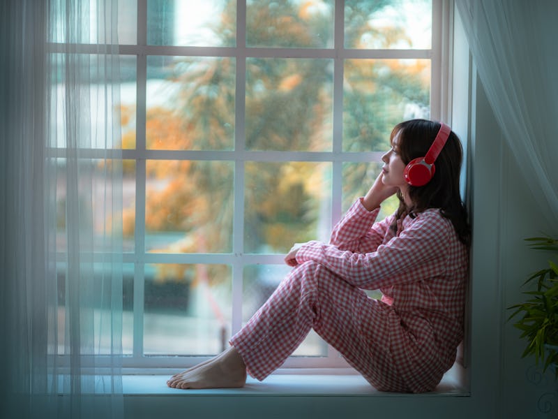 Asian girl sitting lonely listening to music in the window, lifestyle concept, social distancing