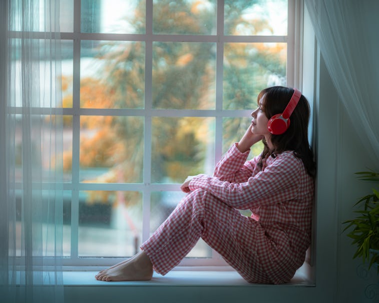 Asian girl sitting lonely listening to music in the window, lifestyle concept, social distancing