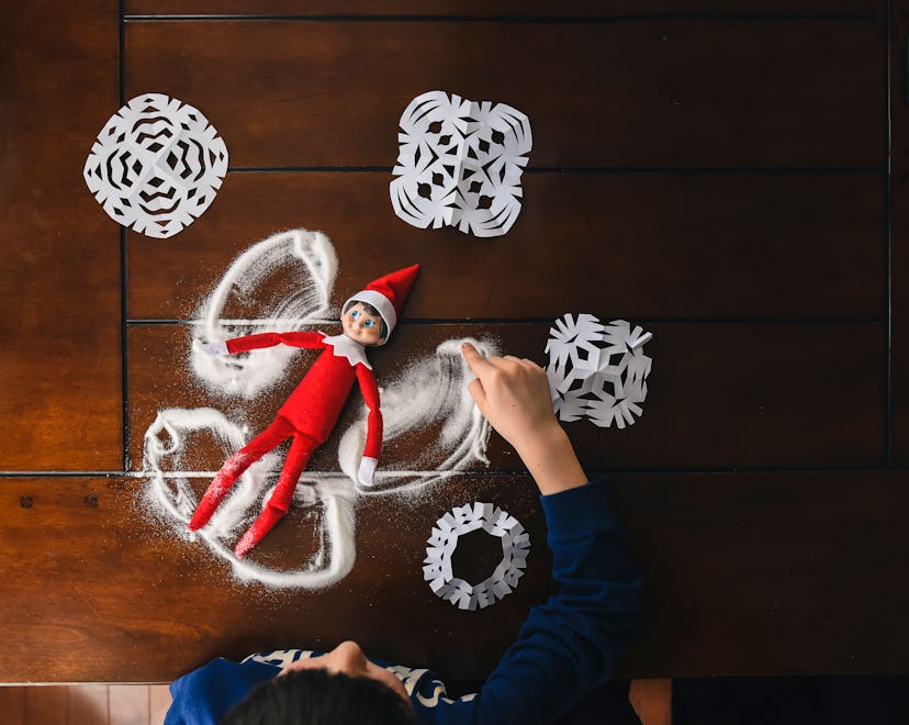 Elf on the Shelf doll on table making snow angel in powdered sugar