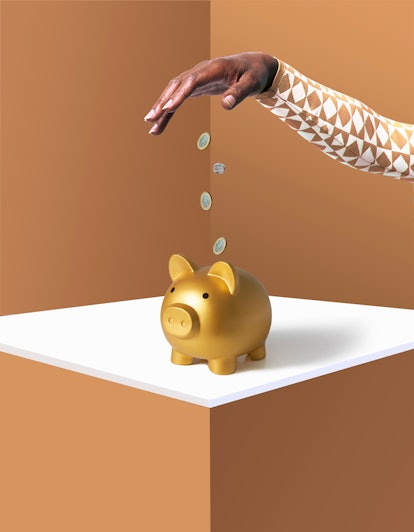 hand dropping pound coins into gold piggy bank against brown background