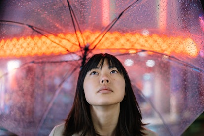 A portrait of a young woman on a rainy day at night in the street while holding an umbrella and look...