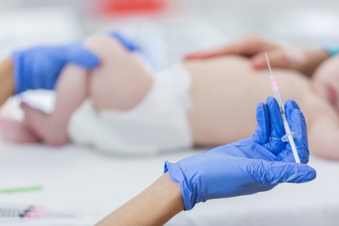Unrecognizable medical professional holds a syringe. She is preparing to give a vaccine to a baby. F...